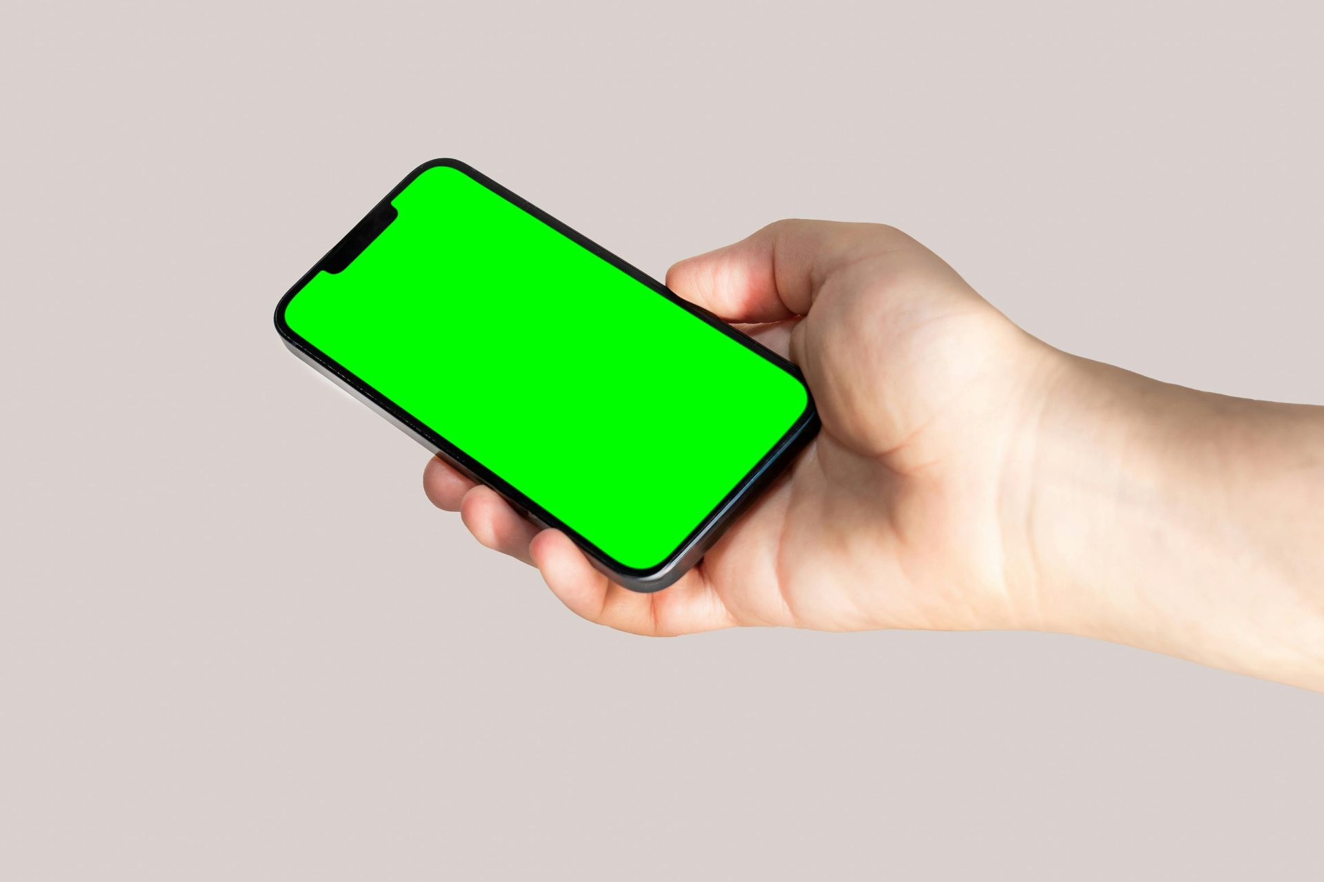 A hand holding a smartphone with a blank green screen perfect for app mockup or design showcase.